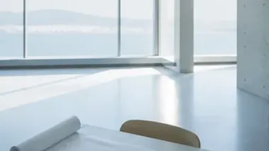 A bright room with a glass wall over the water, a rolled sheet of paper on the table