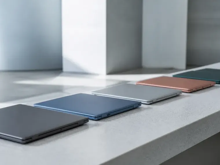 Several closed laptops in different colours lined up on a light table